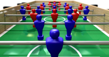 A perspective view of a wooden foosball table showing a blue and red team on a green marked pitch on an isolated white background