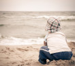 Boy sitting on beach alone looking out to sea