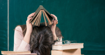 Teacher surrounded by books with head down