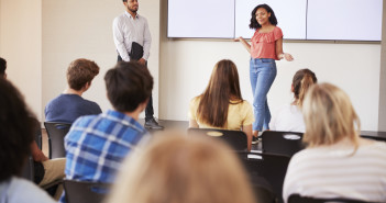 Female Student Giving Presentation To High School Class In Front Of Screen