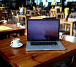 Open laptop computer and cup of coffee lying on a wooden table in cafe bar interior, portable net-book with copy space screen for your information content or text message, distance work via internet